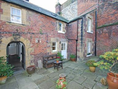 A courtyard with brick walls potted plants and a wooden bench at Dorothy Forster Court in Alnwick
