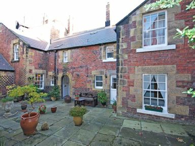 A stone courtyard with potted plants and a wooden bench outside a brick building at Dorothy Forster Court in Alnwick