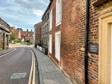 A street with buildings and a sidewalk with a Dorothy Forster Court sign in Alnwick