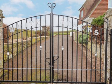 A black metal gate with the words White Stacks at the entrance to a property with stone walls and a driveway at Whitestacks in Bamburgh