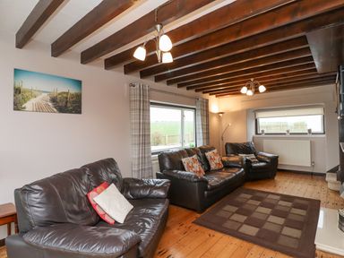 A living room with three black leather sofas a window with curtains and a floor lamp at Whitestacks in Bamburgh