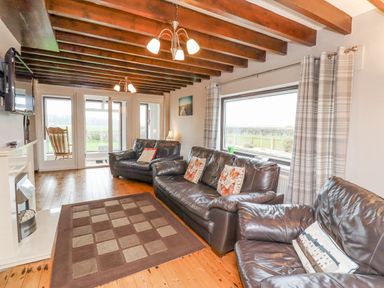 A living room with leather sofas rug wooden floor exposed ceiling beams and large window at Whitestacks in Bamburgh