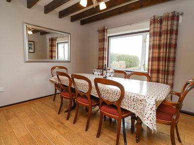 A dining room with a wooden table covered with a patterned tablecloth and six chairs at Whitestacks in Bamburgh
