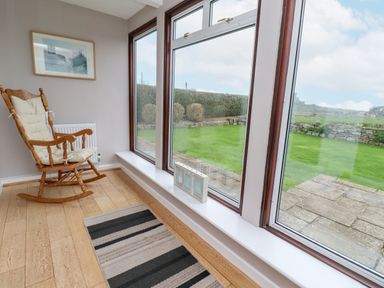 A corner of a room with large windows a wooden rocking chair and a striped rug at Whitestacks in Bamburgh