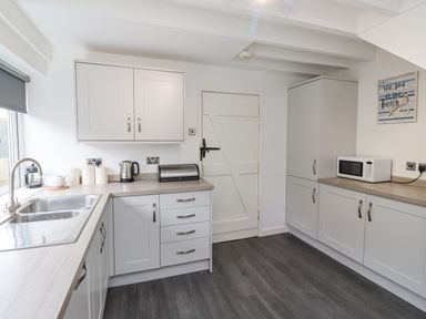 A kitchen with white cabinets a countertop with a kettle microwave toaster and sink at Whitestacks Bamburgh
