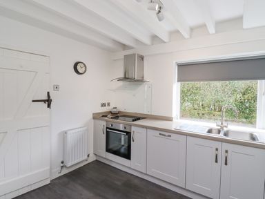 A kitchen with white cabinets a stainless steel oven and hood a double sink and a window with a grey blind at Whitestacks in Bamburgh