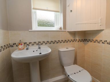 A bathroom with a pedestal sink with soap a toilet and a window above at Whitestacks in Bamburgh