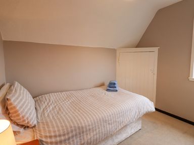 A bedroom with a single bed with striped bedding folded towels on the bed and a small door on the wall at Whitestacks Bamburgh