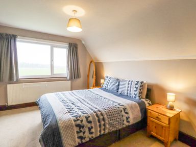 A bedroom with a bed a bedside table with a lamp a window with curtains and a standing mirror at Whitestacks in Bamburgh
