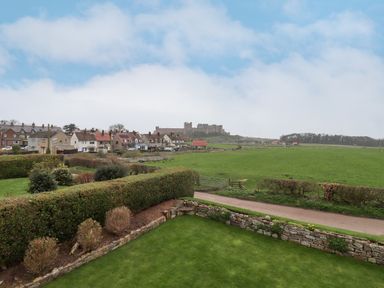 A green garden with stone walls and bushes with houses and a castle in the background at Whitestacks in Bamburgh