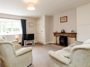 A sitting room with two armchairs a television on a stand a fireplace with a clock and framed pictures on the walls at Bilton Farm Cottage No1 in Alnmouth