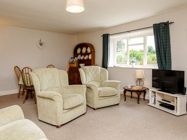 A living room with armchairs a television on a stand a side table with a lamp and a dining table with chairs at Bilton Farm Cottage No1 in Alnmouth