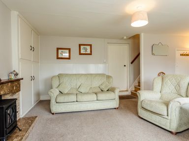 A living room with a sofa and armchair near a fireplace and staircase at Bilton Farm Cottage No1 in Alnmouth