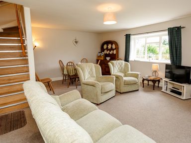 A living room with beige sofas a wooden staircase a dining table with chairs and a television at Bilton Farm Cottage No1 in Alnmouth