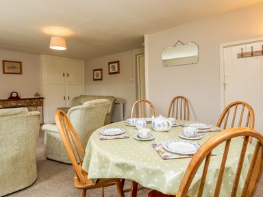 A dining area with a table set for tea and chairs with an adjoining living area with armchairs and a fireplace at Bilton Farm Cottage No1 in Alnmouth