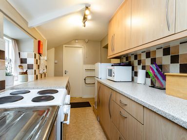A narrow kitchen with wooden cabinets a stove a microwave a refrigerator and tiled backsplash at Bilton Farm Cottage No1 in Alnmouth