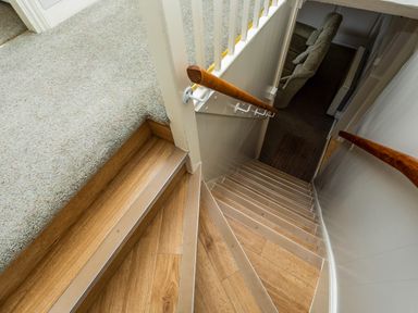 A staircase with wooden steps and handrails leading down to a room with a carpet and sofa at Bilton Farm Cottage No1 in Alnmouth