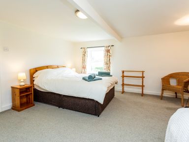 A bedroom with a double bed next to a window with floral curtains and wooden furniture at Bilton Farm Cottage No1 in Alnmouth