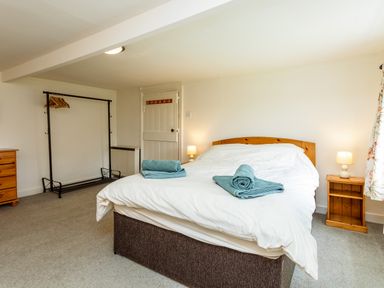 A bedroom with a bed white bedding blue towels wooden side tables lamps and a clothing rack at Bilton Farm Cottage No1 in Alnmouth