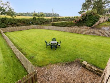 A fenced grassy yard with a round table and four chairs in the center at Bilton Farm Cottage No1 in Alnmouth