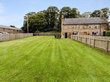 A large grassy garden with plastic chairs and a stone house with multiple windows at Bilton Farm Cottage No1 in Alnmouth