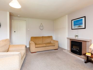 A living room with two beige sofas a fireplace and a framed beach picture at Bilton Farm Cottage No2 Alnmouth