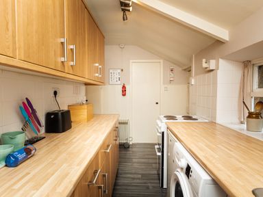 A narrow kitchen with wooden cabinets and countertops a washing machine stove and kitchen utensils at Bilton Farm Cottage No2 in Alnmouth
