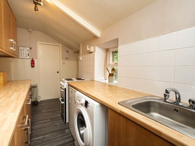 A narrow kitchen with wooden countertops a washing machine a sink stove cabinets and a small window at Bilton Farm Cottage No2 Alnmouth