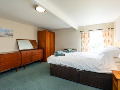 A bedroom with a bed, wooden dresser, wardrobe, and window with floral curtains at Bilton Farm Cottage No2 in Alnmouth