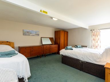 A bedroom with two beds a wooden dresser and wardrobe and floral curtains at Bilton Farm Cottage No2 in Alnmouth