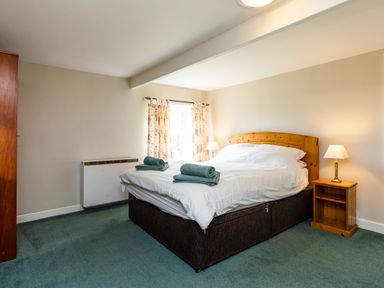 A bedroom with a double bed with white linens and folded towels on top next to wooden nightstand with lamp at Bilton Farm Cottage No2 in Alnmouth
