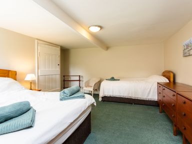 A bedroom with two beds a white armchair and a wooden dresser at Bilton Farm Cottage No2 in Alnmouth