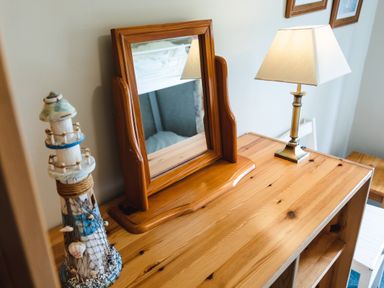 A wooden dresser with a framed mirror a decorative lighthouse and a table lamp at Bilton Farm Cottage No2 in Alnmouth