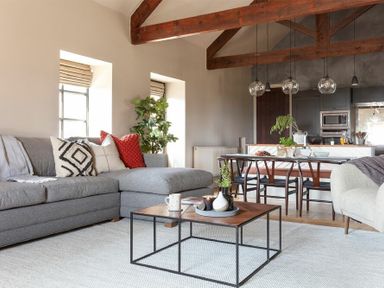 A living room with a gray sectional sofa and a wood and metal coffee table near a dining area with a wooden table and chairs under exposed wooden beams at Lantern View Eglingham