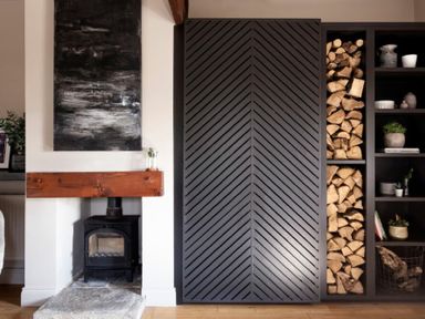 A fireplace with a wood-burning stove and a wooden mantel next to a shelf with firewood and decorative items at Lantern View in Eglingham