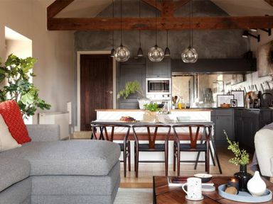 An open plan living room and kitchen with wooden beams wooden dining chairs and a gray sofa at Lantern View in Eglingham