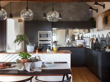 A kitchen with dark cabinets a wooden countertop a dining table with plants and a lit candle at Lantern View in Eglingham