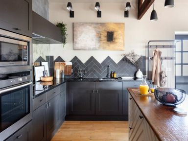 A kitchen with black cabinets and appliances wooden countertop and tiled backsplash at Lantern View in Eglingham