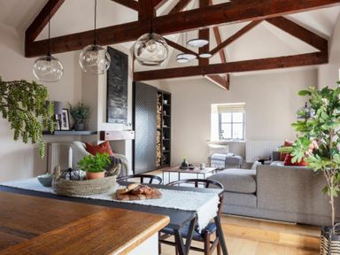 An open living room with wooden beams a gray sofa and dining table with plants at Lantern View in Eglingham