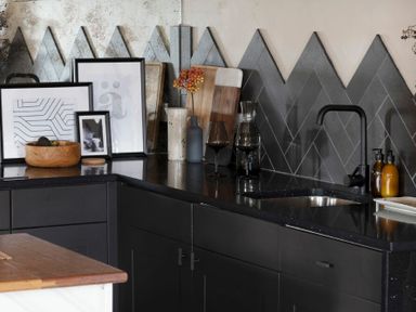A kitchen corner with black cabinets a black countertop a black faucet two bottles soap dispensers framed artwork cutting boards and a bowl with fruit at Lantern View in Eglingham