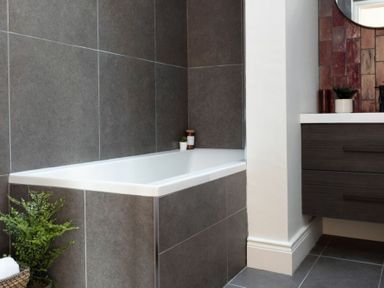 A bathroom with a bathtub surrounded by gray tiles and a dark brown vanity unit at Lantern View in Eglingham