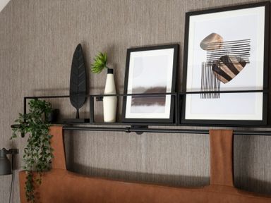 A black metal shelf above a brown leather headboard with framed abstract art and decorative plants at Lantern View in Eglingham