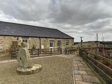 An exterior view of a stone building with a gravel courtyard and a stone circular structure at Lantern View in Eglingham