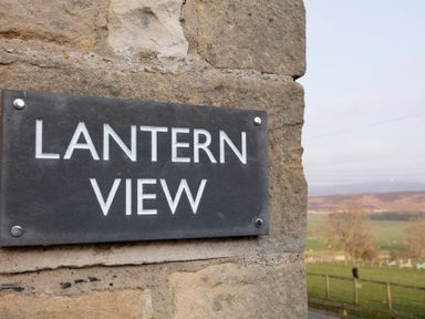 A stone wall with a sign reading Lantern View overlooking a rural landscape with fields and trees at Lantern View in Eglingham