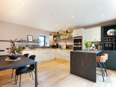 A kitchen with white cabinets black island wooden floor and a dining table with chairs at The Bolthole in Eglingham
