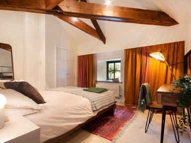 A bedroom with wooden beams a bed a window with orange curtains and a wooden desk at The Bolthole in Eglingham