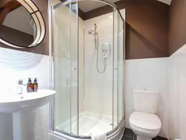A bathroom with a corner shower enclosure a toilet a pedestal sink and a round mirror at The Bolthole in Eglingham