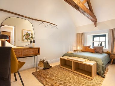 A bedroom with a bed sofa cushions wooden table mirror and window with curtains at The Bolthole in Eglingham