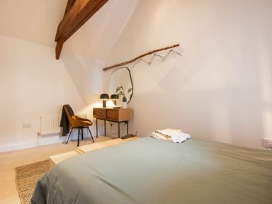 A bedroom with a bed folded towels a chair desk mirror lamp and a wooden hanger on the wall at The Bolthole in Eglingham