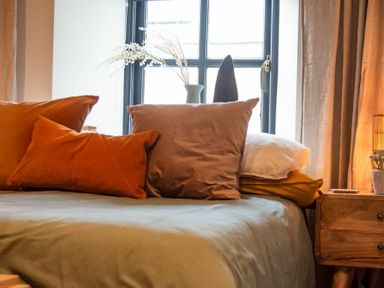 A bed with multiple pillows next to a wooden nightstand and a window with curtains at The Bolthole in Eglingham